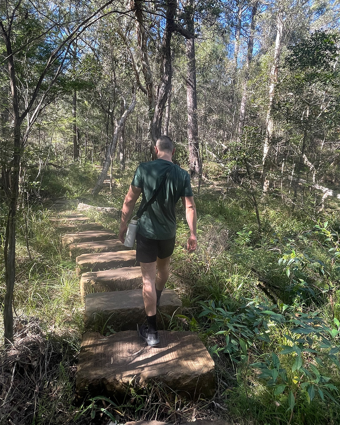 a man walking over stepping stones at brisbane hiking spot glasshouse mountains
