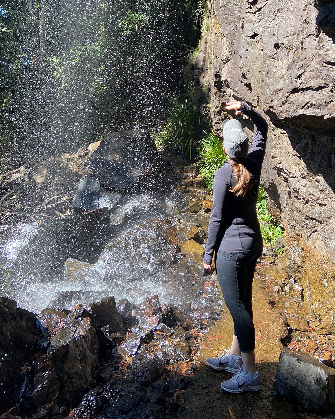 a woman standing under a waterfall at brisbane hiking spot springbrook 