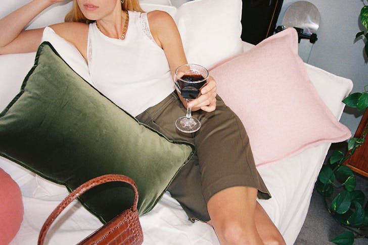 A woman reclining with some velvet cushions and a glass of wine. 