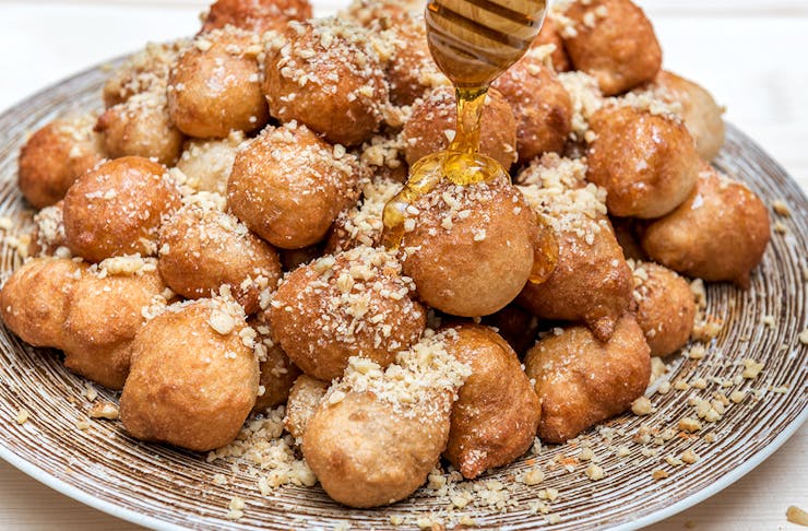 A pile of golden honey puffs on a plate being drizzled in honey