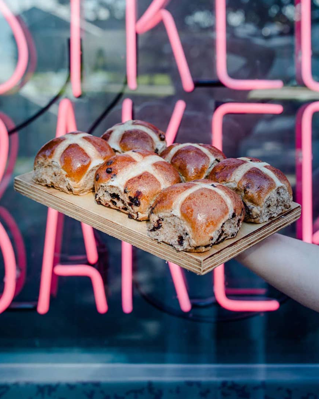 person holds hot cross buns in front of neon sign