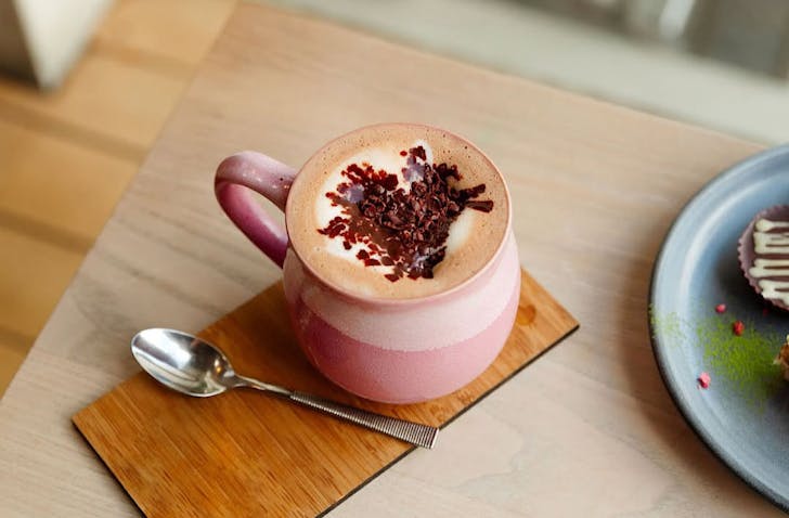 A cute pink mug of hot cacao decorated with chocolate sprinkles in the shape of a heart. 