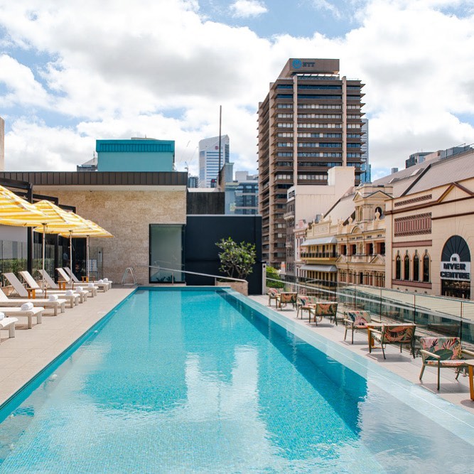 a rooftop pool with daybeds and tables