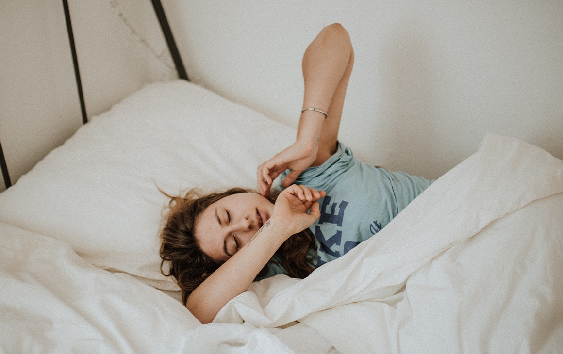 woman wearing a blue shirt lying bed alone with her eyes closed