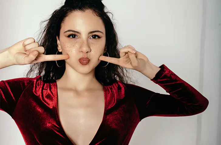 a woman in a red dress pointing at her cheeks