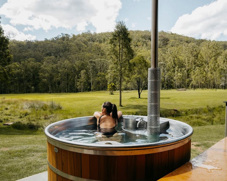 a woman enjoys a countryside view from a hot tub at a huch tiny home in the hunter valley