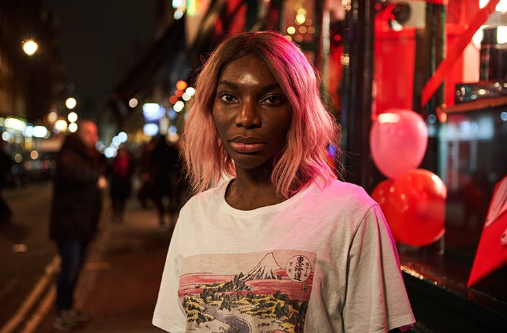 Michaela Coel in the series I May Destroy You, standing on a brightly-lit street at night.