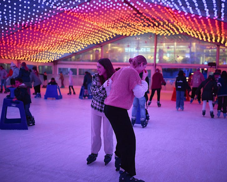 People enjoy the Aotea Ice Rink under bright colourful pink, purple, yellow and orange lights.