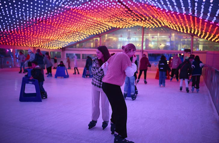 People enjoy the Aotea Ice Rink under bright colourful pink, purple, yellow and orange lights.