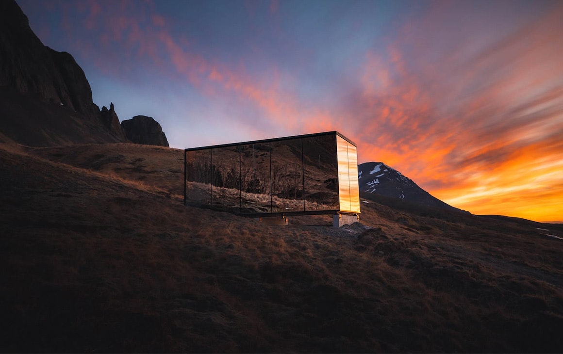 a mirrored cabin at sunset in front of a mountain, one of iceland's incredible airbnbs