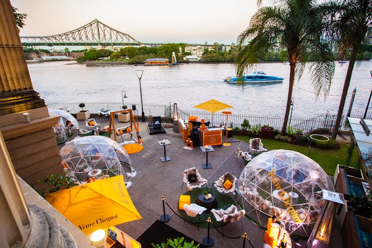 several clear plastic igloos by the river overlooking the Story Bridge