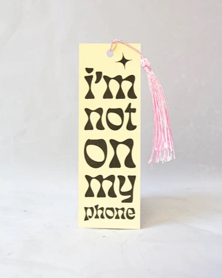 A paper bookmark with the words Not On My Phone in a groovy typography, plus a fun pink tassel
