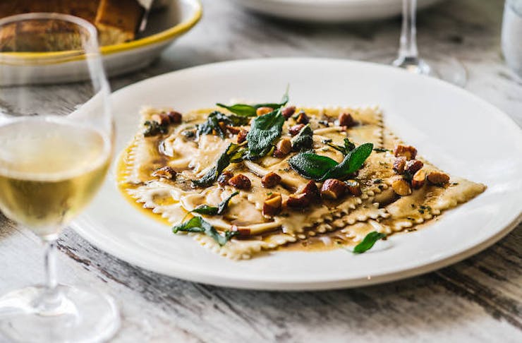 A plate of ravioli from Capriccio Osteria drizzled with olive oil, nuts and thyme with a glass of white wine.