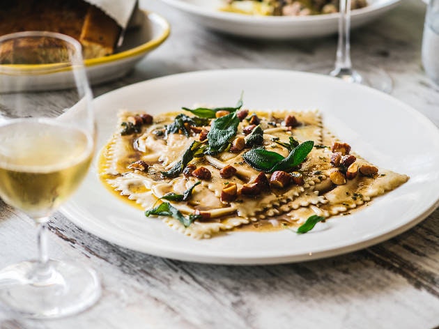 A plate of ravioli from Capriccio Osteria drizzled with olive oil, nuts and thyme with a glass of white wine.