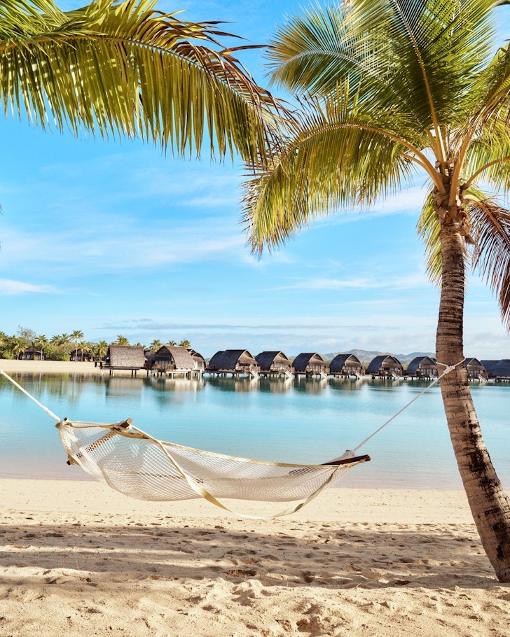 A hammock sits between two palm trees a lagoon