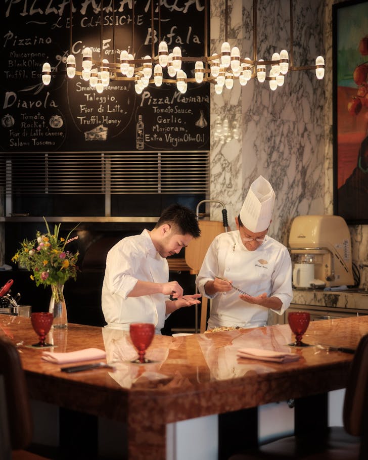 Two chefs wearing chef hats serve up a pizza.