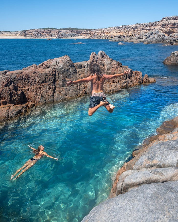 A person jumps off a rocky outcrop into a pool of water