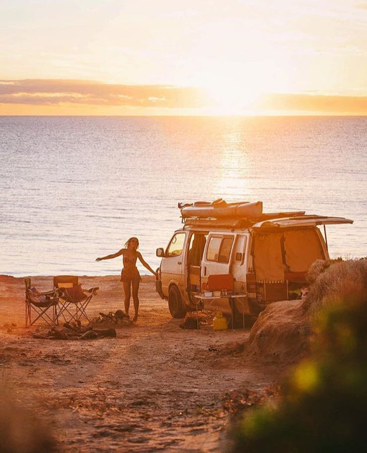 A person, beside a camper on the beach at sunset