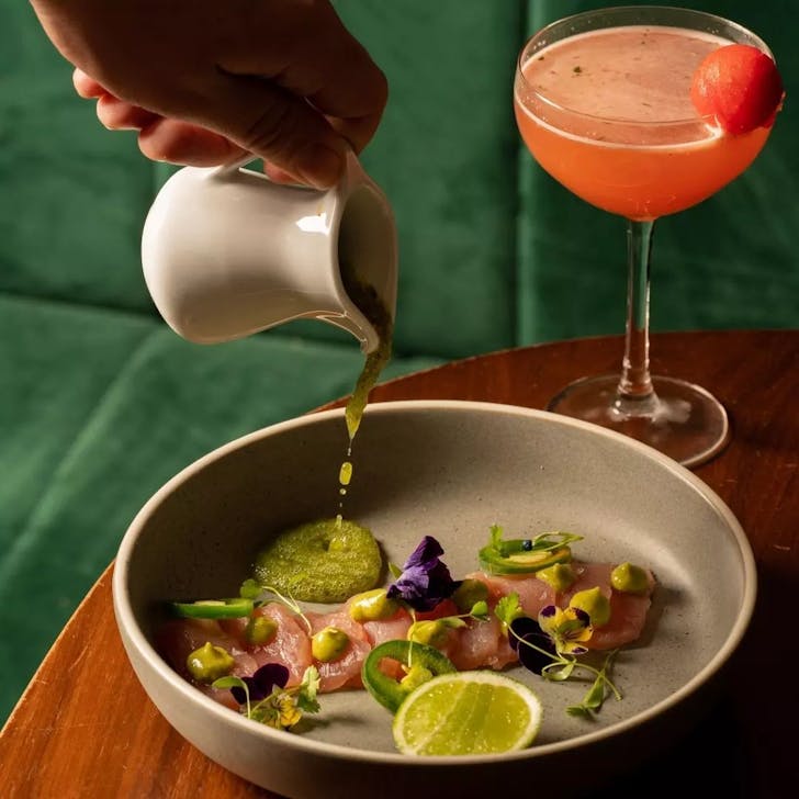 cocktail and plate of food with hand pouring sauce, from employees only restaurant in sydney