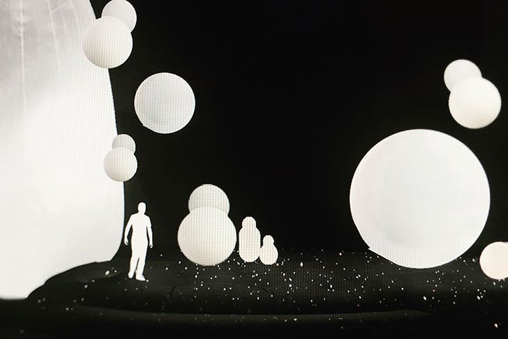 Inflatable, illuminated spheres surround a person standing on their own in a dark room.