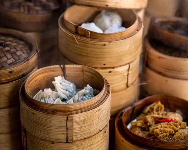 A picture of multiple stacked bamboo steamer trays with different kinds of dumplings inside. The picture is taken from side view.