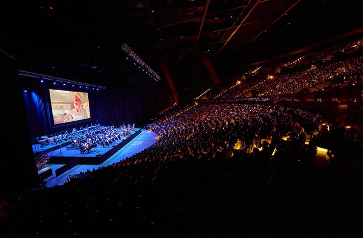 An orchestra playing in front of giant screen.