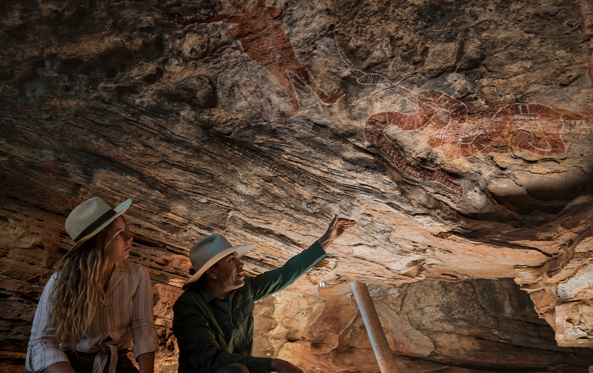 two people looking up at rock art in a cave