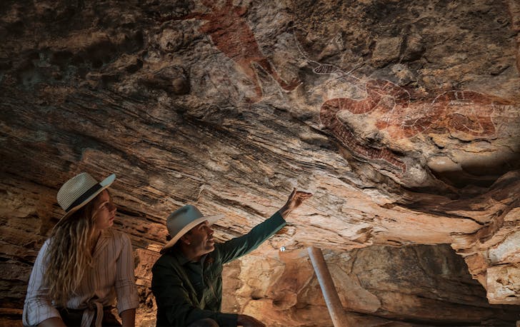 two people looking up at rock art in a cave