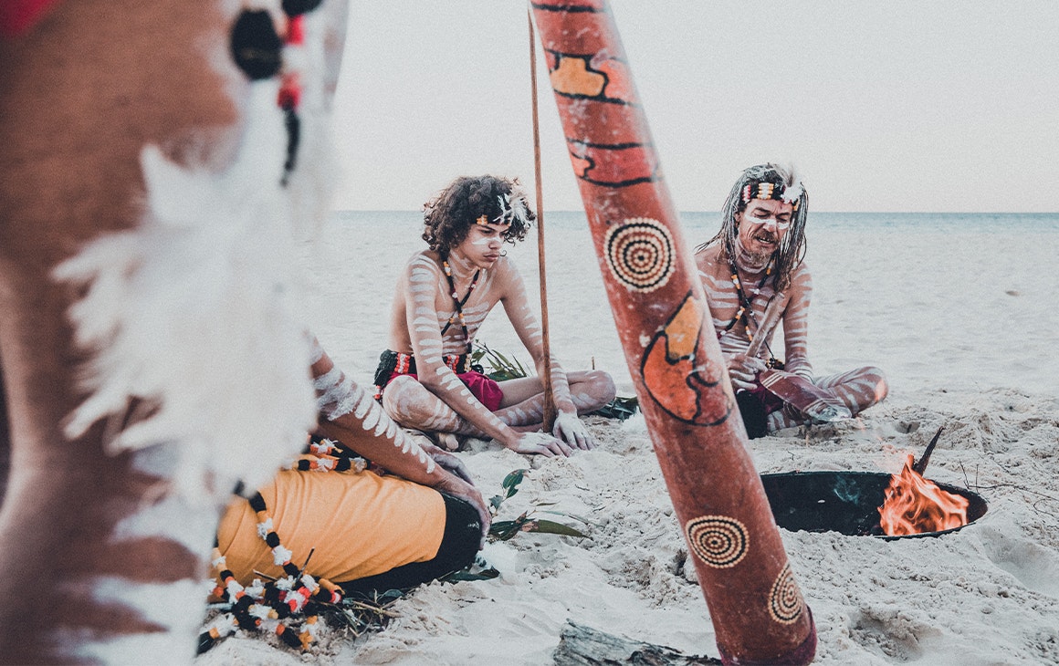 several people in indigenous paint and outfits sitting on a beach