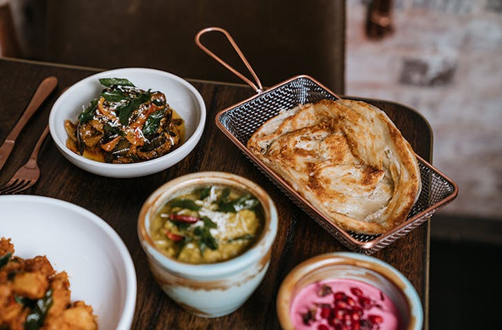 Several plates of Sri Lankan food surrounded by bronze cutlery.