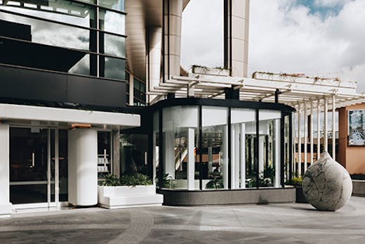 A cafe situated by a large concrete pillar. A concrete sphere sits next to the cafe's outdoor seating.