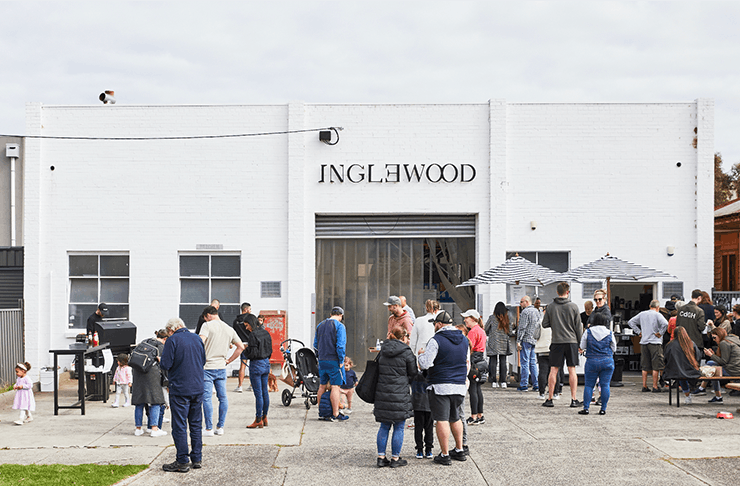 The exterior of Inglewood roastery a white brick building with people lining up out front. 