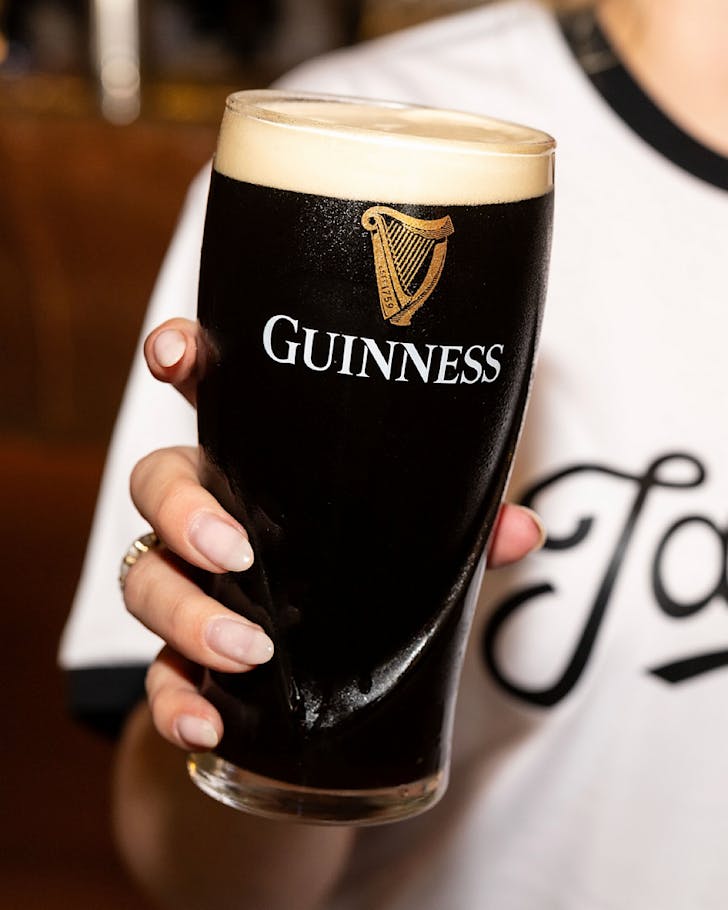 Someone in a white t-shirt holds up a freshly-poured Guinness.