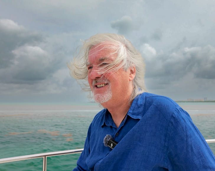 James May on a boat in the middle of the ocean, his hair blowing to one side in the wind.