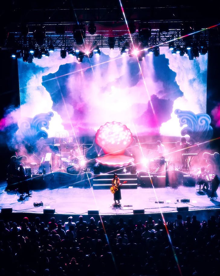 Japanese Breakfast perform to a massive crowd on a pink, dreamily produced stage with bright effects. 