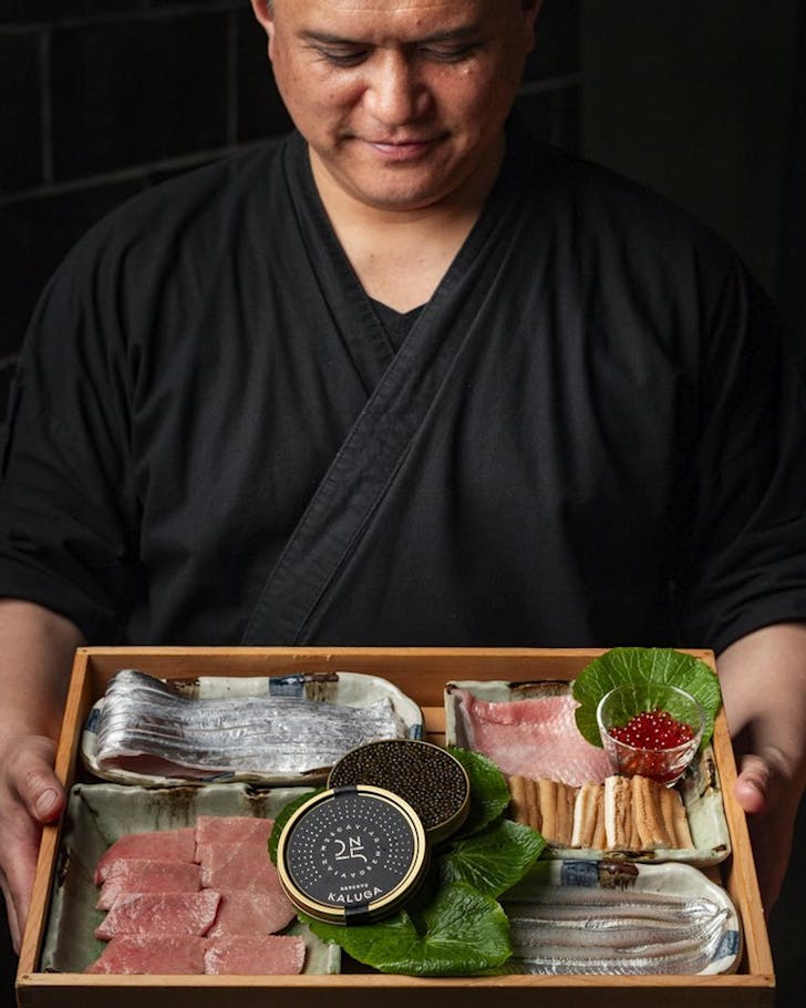 a japanese chef holds a tray of raw seafood and caviar