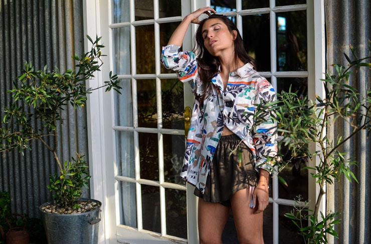 A woman wearing a colourful t-shirt leaning on french doors. 
