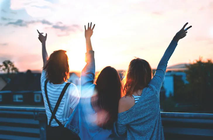 Three people throwing peace signs to a sunset at a party. 