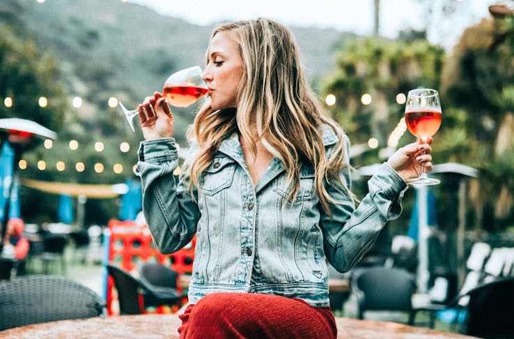 A woman sitting on a table holding two glasses of rose wine. 