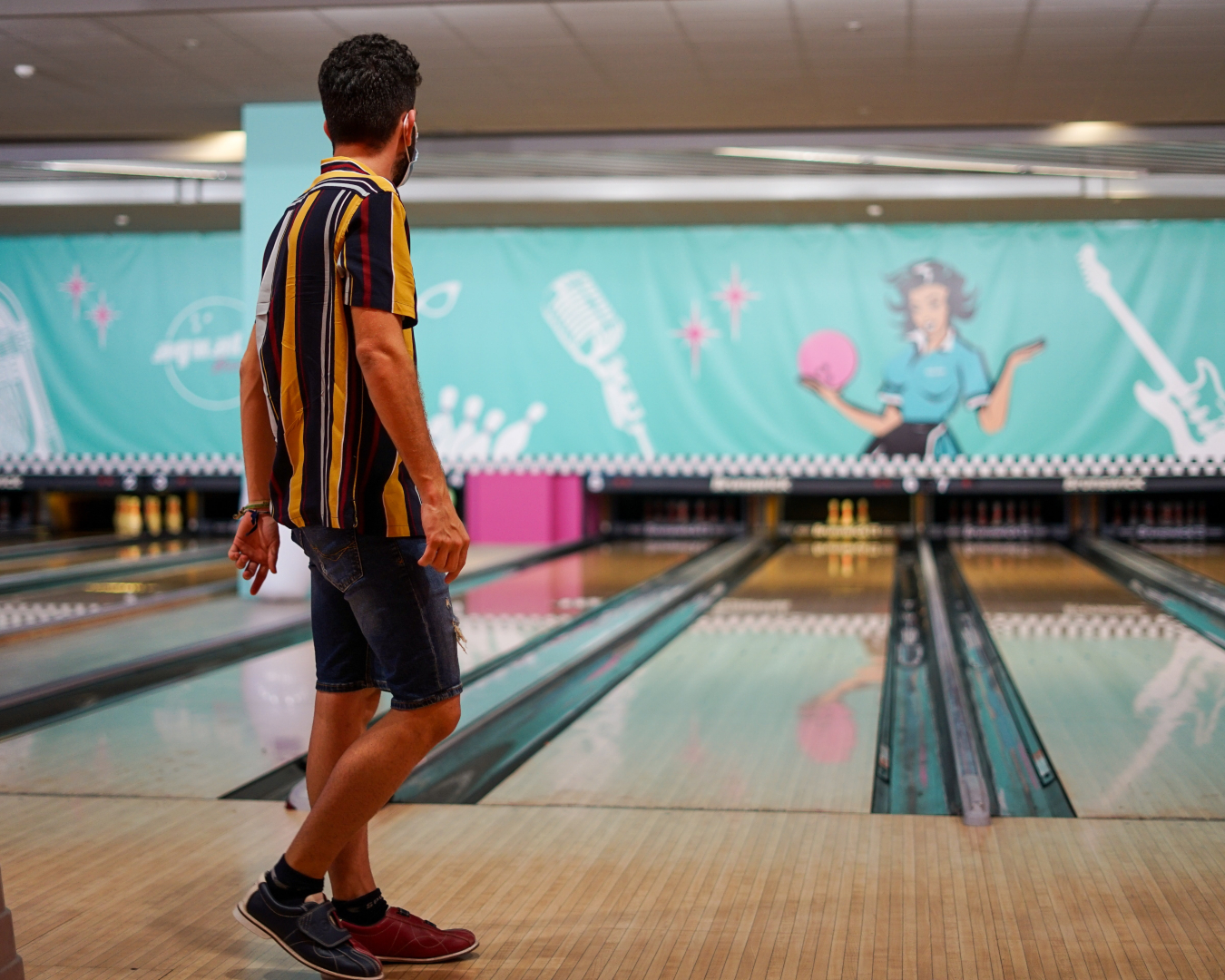 The bright lights and shiny floors of the bowling alley are showcased as a man steps up to bowl