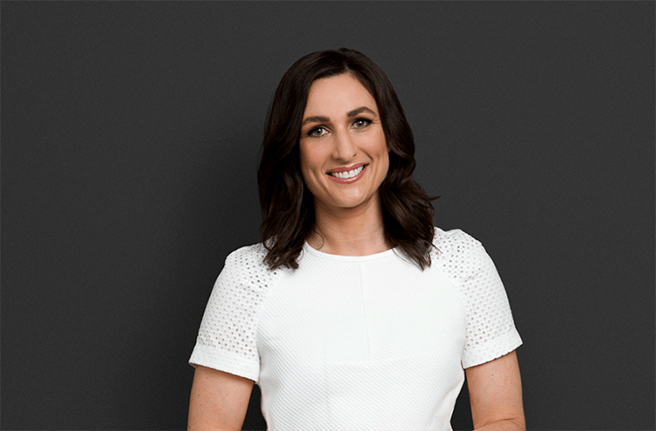 A portrait of private investigator Julia Robson, who's wearing a white t-shirt and standing in front of a grey background.