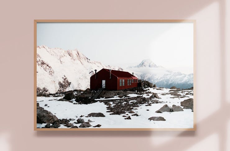 A snow topped cabin in New Zealand framed on a wall. Photo is by Jackson Loria.
