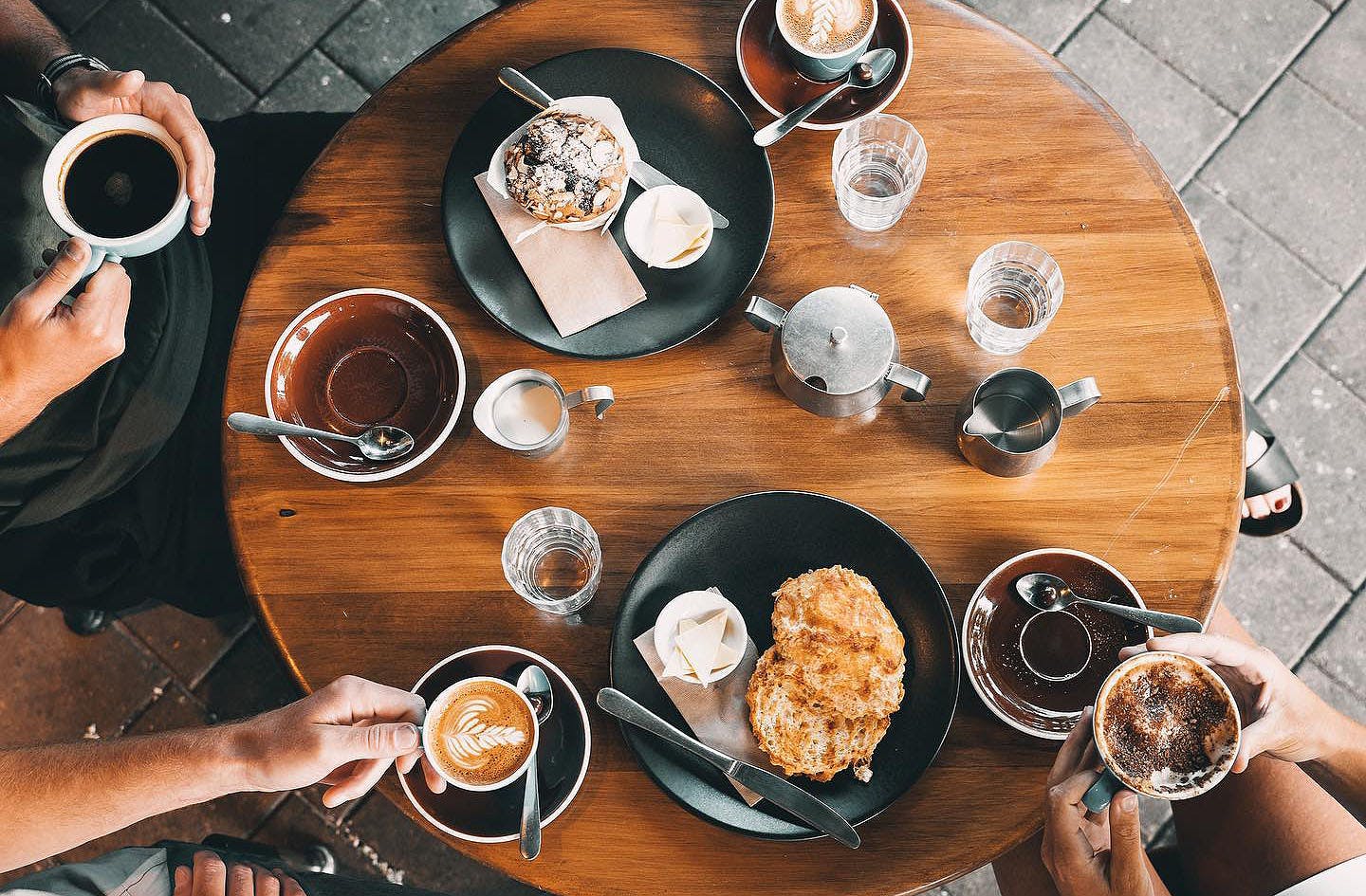 four cafe-goers seated around a wooden table enjoying coffee and scones at Kai Whakapai Cafe 