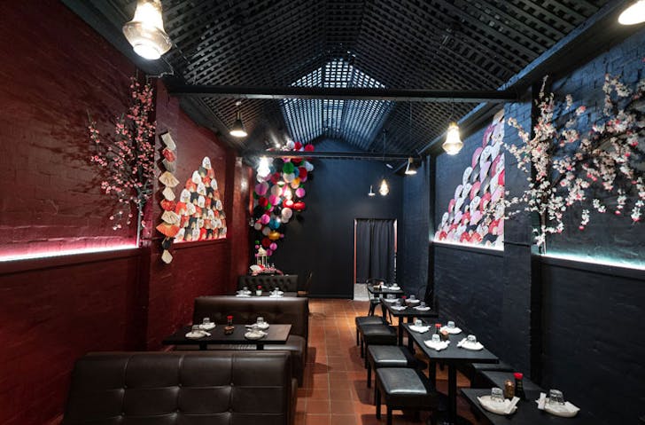 The enclosed courtyard space at Kaiza Izakaya with moody black and red walls that have been adorned with cranes, fans, and lanterns. 