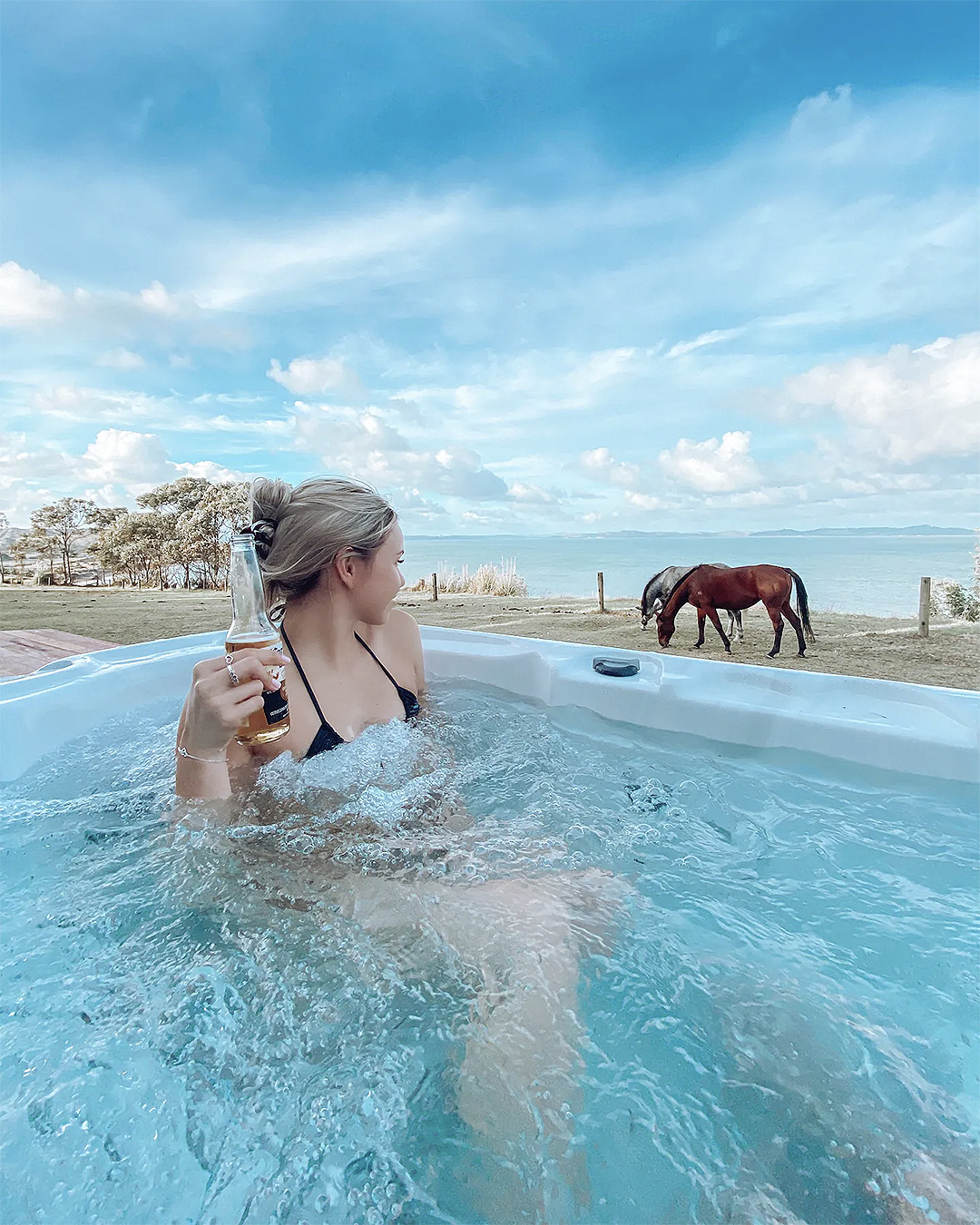 A woman looks at horses grazing from a hot tub.