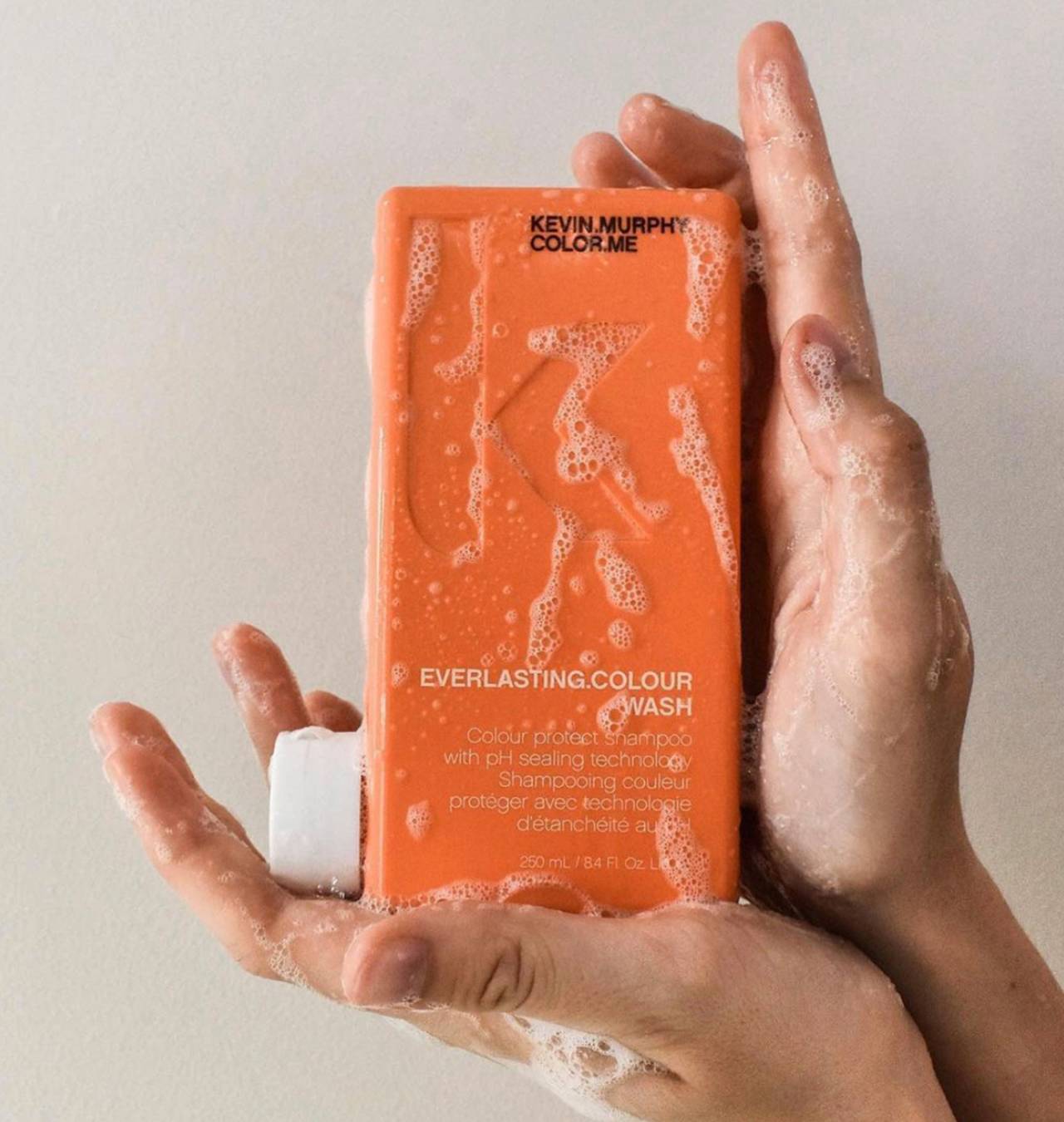 hands with soap sudds holding orange shampoo bottle
