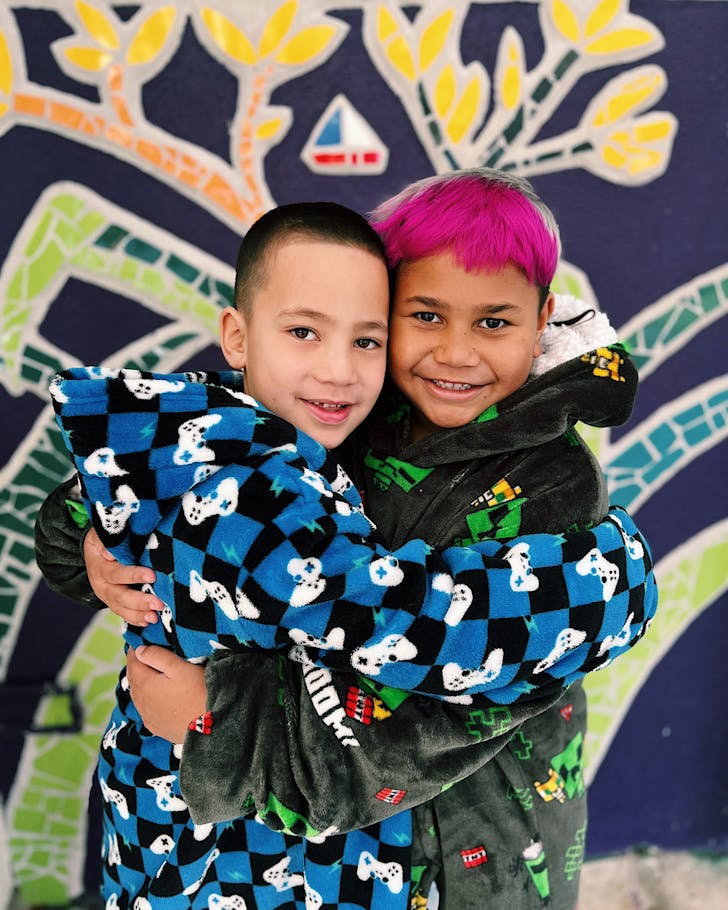 Two kids in cosy dressign gowns share a warm hug.