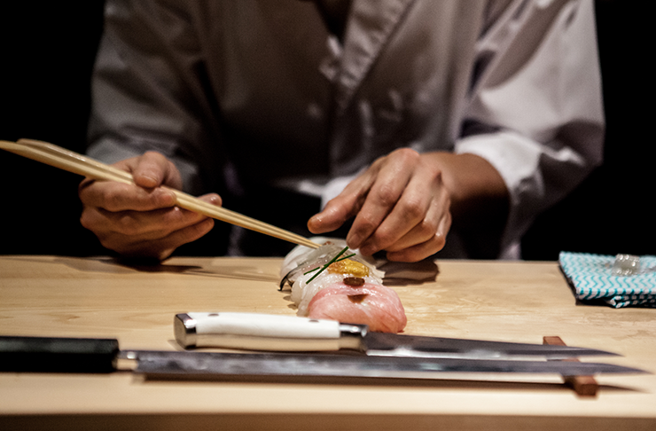 A chef preparing sushi on a wooden bar with a knife at a best Japanese restaurant in Melbourne.