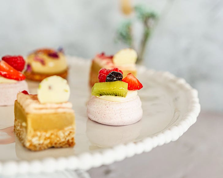 Ginger crunch and fruit-topped pavlova in miniature format on a white cake stand.