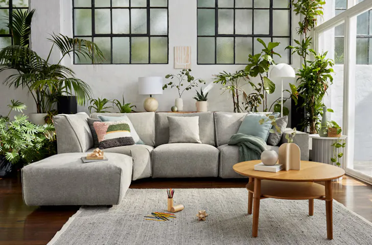 A grey modular sofa surrounded by lush green plants